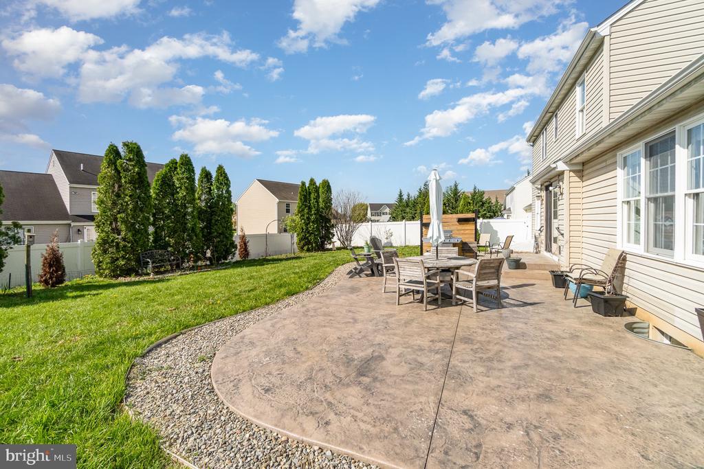 Backyard patio with outdoor dining set beside a green lawn and fenced yard.