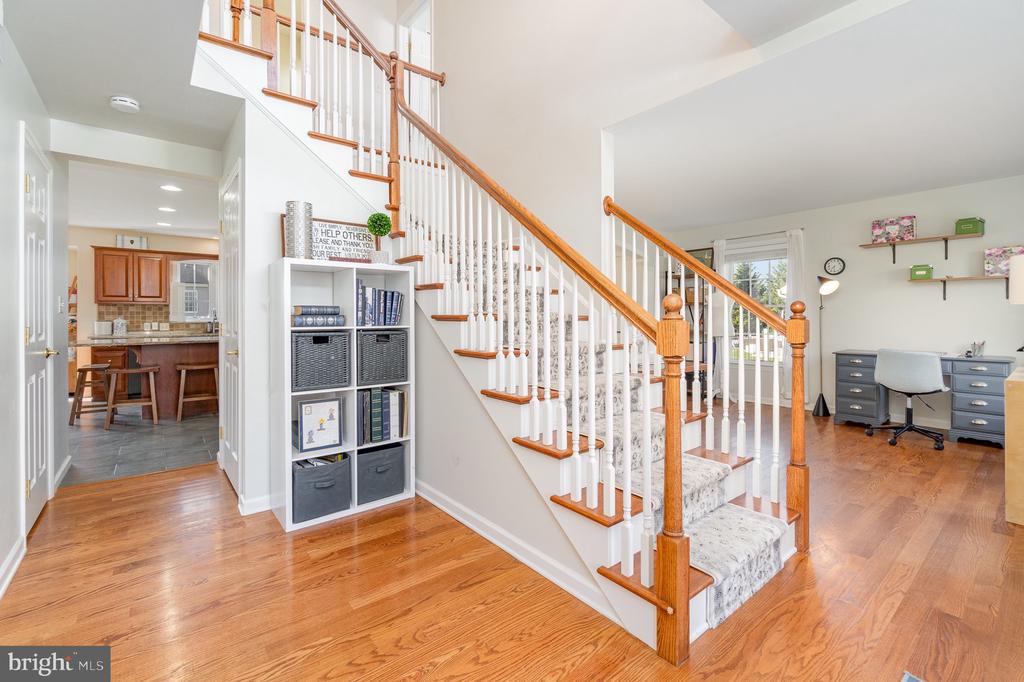 Entry hall with a carpeted staircase, wood handrail, hardwood floors, and an adjoining home office.