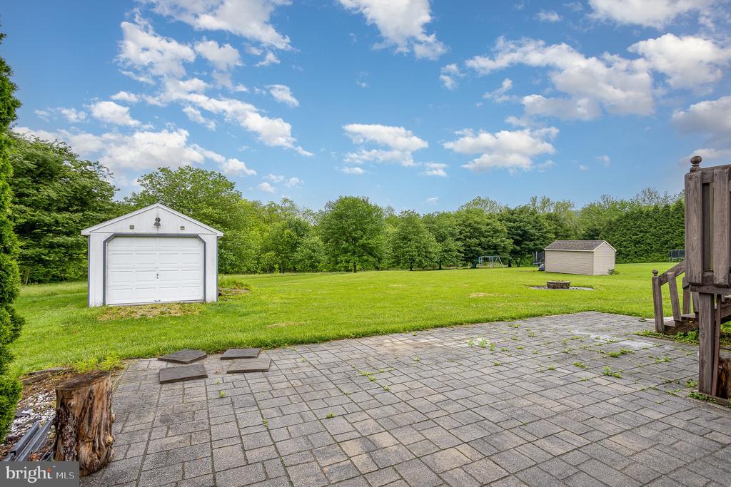 Backyard lawn with two detached sheds and a broad paved patio.