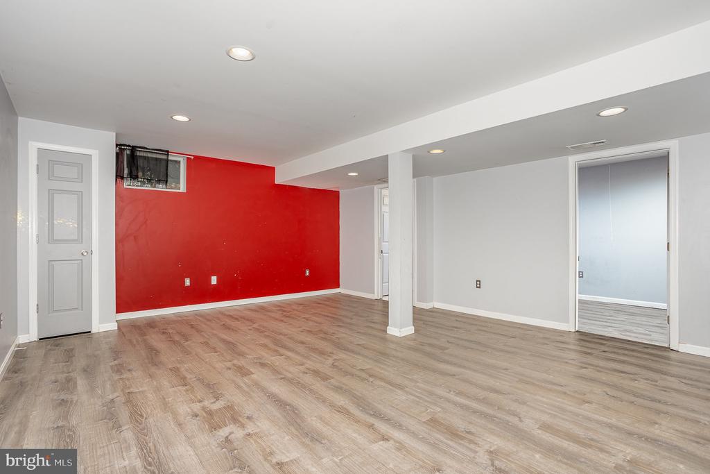 Finished basement with wood-look flooring, a red accent wall, recessed lights, and a support column.