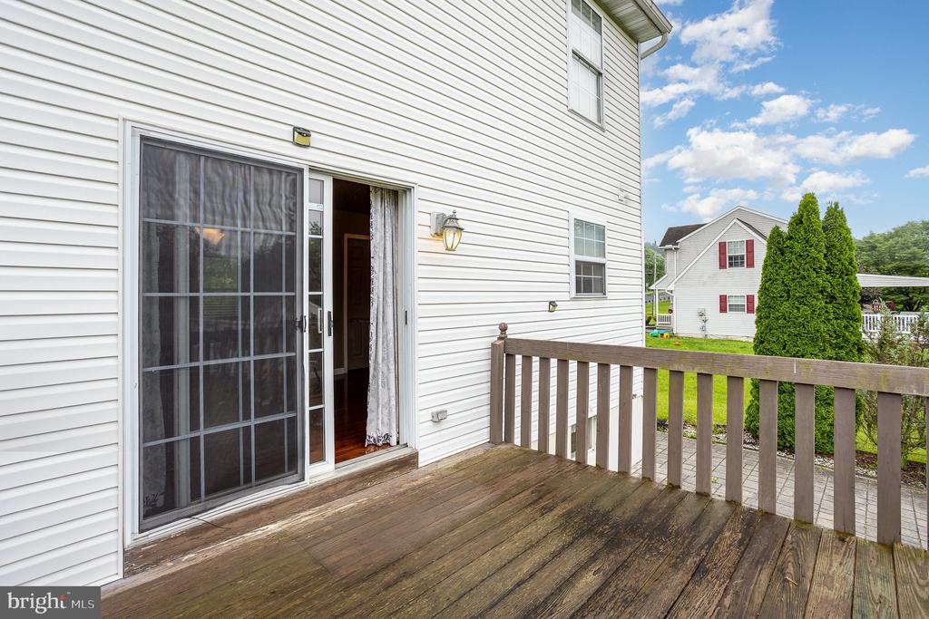 Wooden deck beside a white-sided home, with an open sliding door and neighboring house beyond the railing.