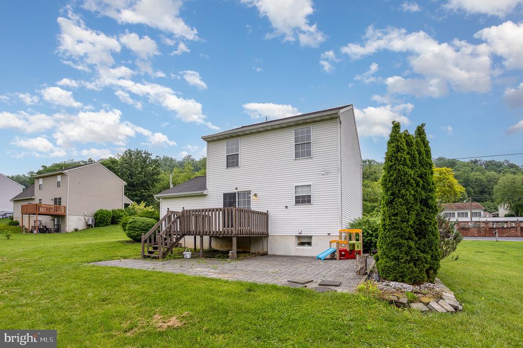 Rear exterior of a two-story white home with a raised deck, patio, and lawn.