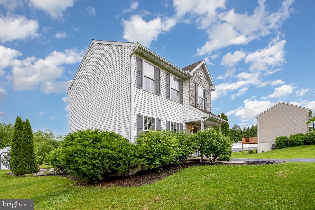 Two-story white-sided home with stone gable, covered porch, and landscaped front yard.