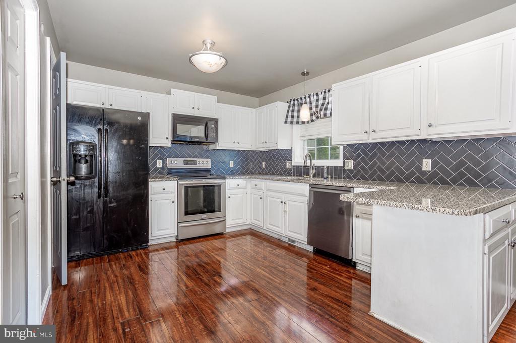 Kitchen with white cabinetry, dark herringbone backsplash, stainless appliances, and glossy wood flooring.