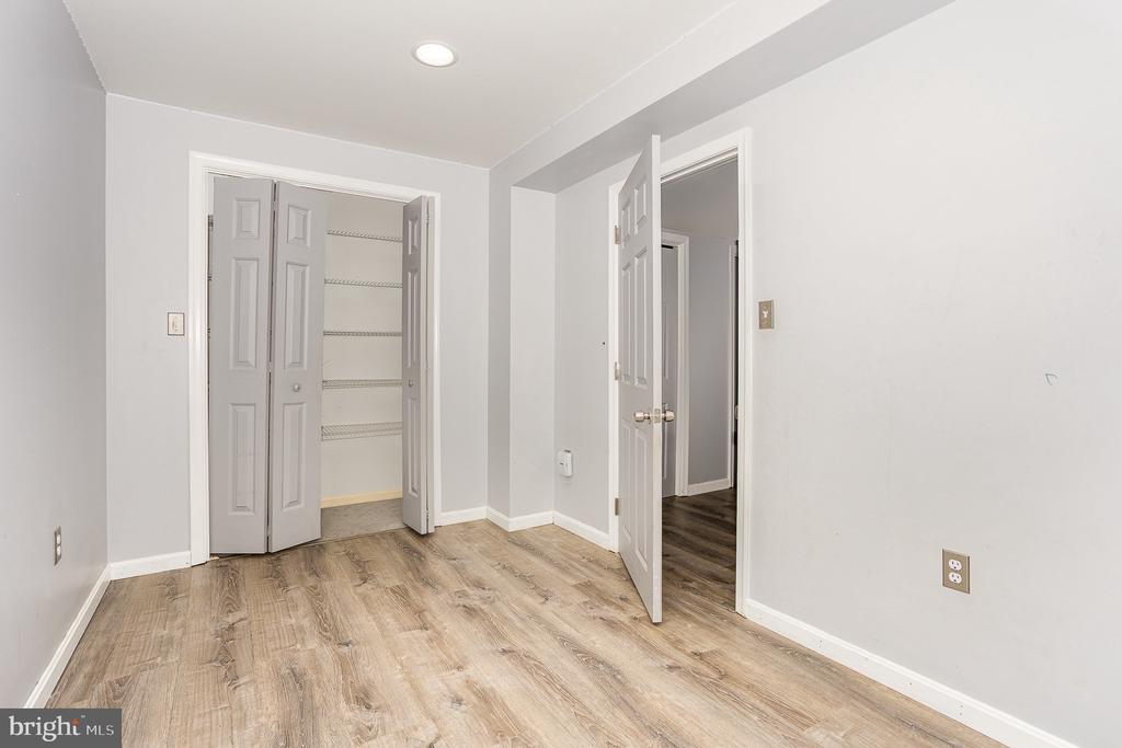 Empty room with wood-look flooring, an open closet, and a doorway to an adjoining space.