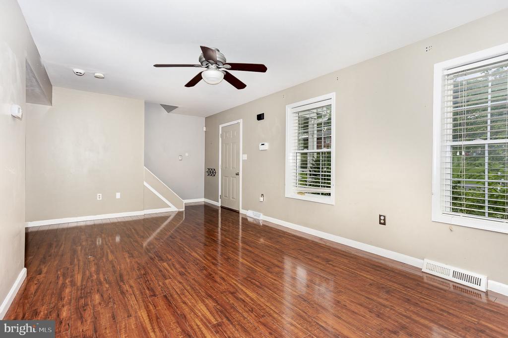 Empty living room with glossy hardwood floors, two bright windows, and a staircase.