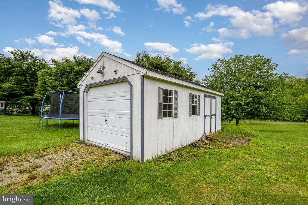 White detached garage with a large front door, side windows, and a trampoline nearby.
