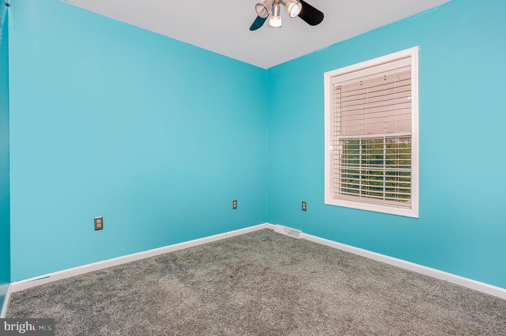 Empty bedroom with turquoise walls, gray carpet, a window with blinds, and a ceiling fan.