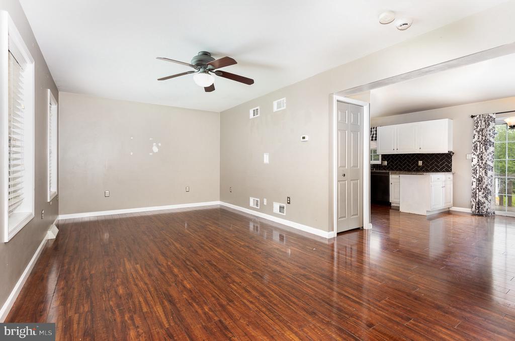 Unfurnished living room with dark hardwood floors and a ceiling fan, opening to a white-cabinet kitchen.