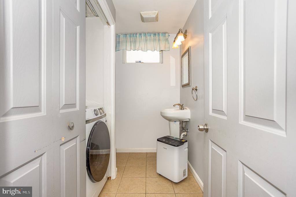 Laundry room with a front-loading washer, utility sink, and small high window with a blue-green valance.