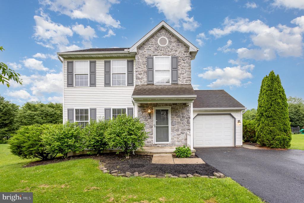 Two-story home with a stone facade, gray shutters, attached garage, and landscaped front lawn.