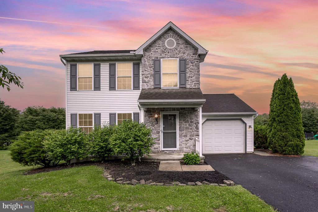 Two-story stone-front house with dark shutters, an attached garage, and a landscaped lawn at dusk.