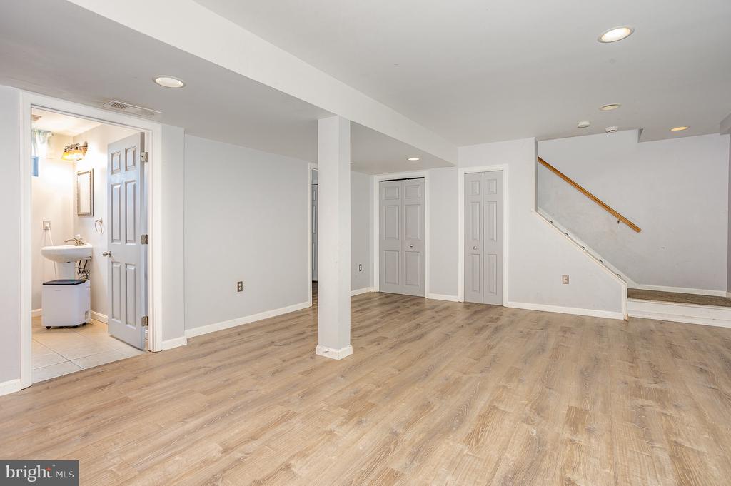 Finished basement with light wood-look flooring, staircase, and an open bathroom doorway.
