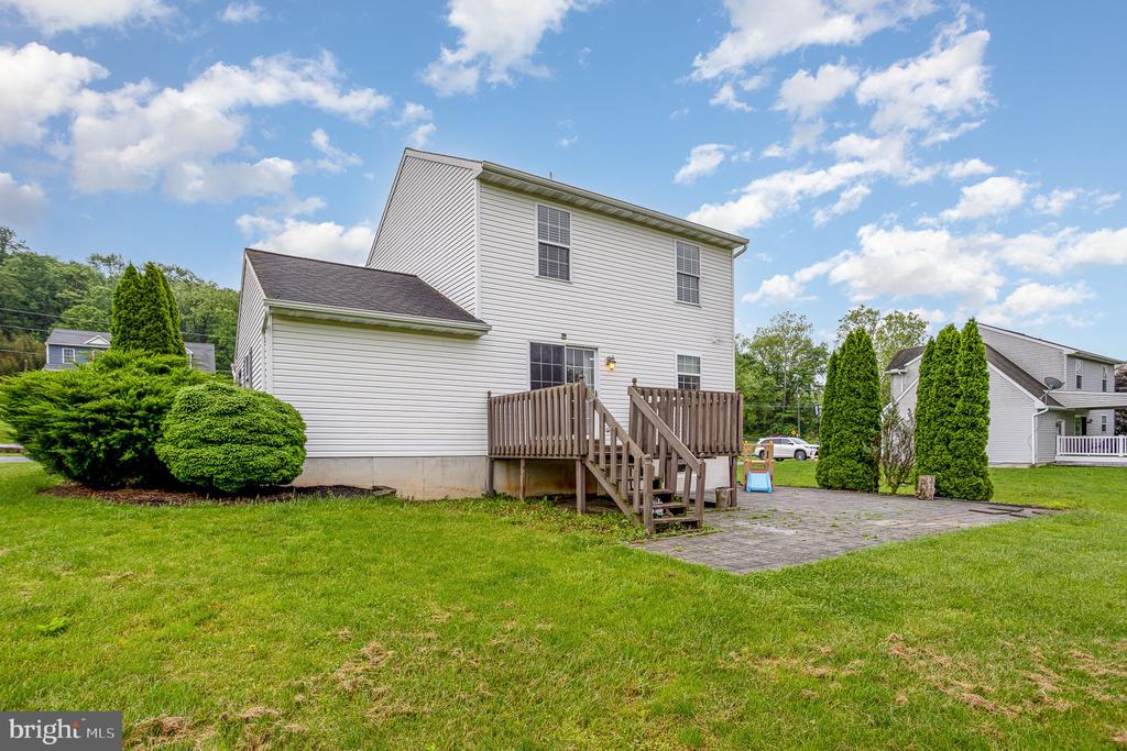 Rear of a two-story white house with a wooden deck, paved patio, and broad lawn.