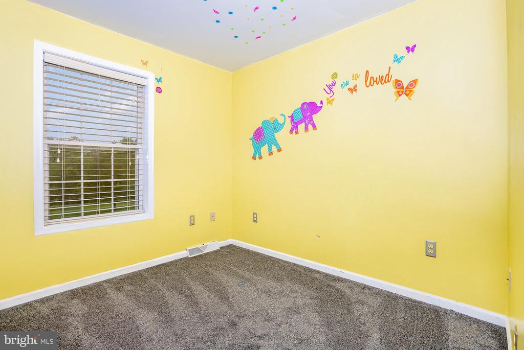 Empty yellow bedroom with gray carpet, a window with blinds, and colorful elephant wall decals.