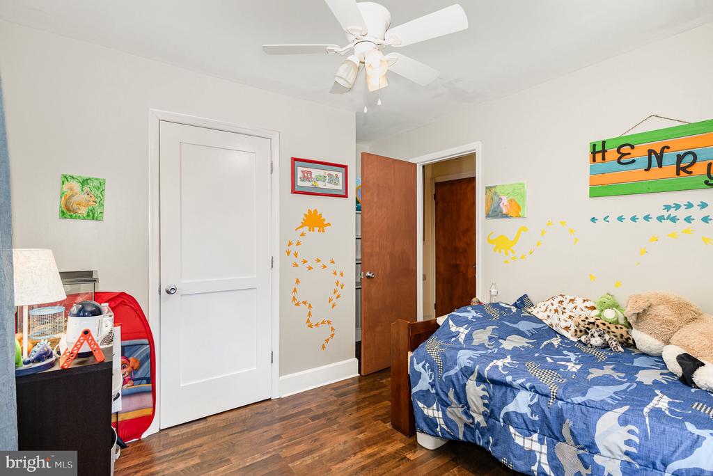 Bedroom with a blue dinosaur-print bedspread, hardwood floors, and colorful dinosaur wall decorations.