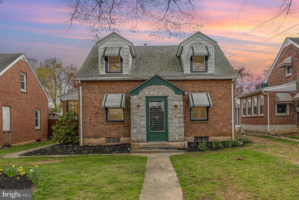 Brick house with a stone entry, green door, and two dormers at dusk.