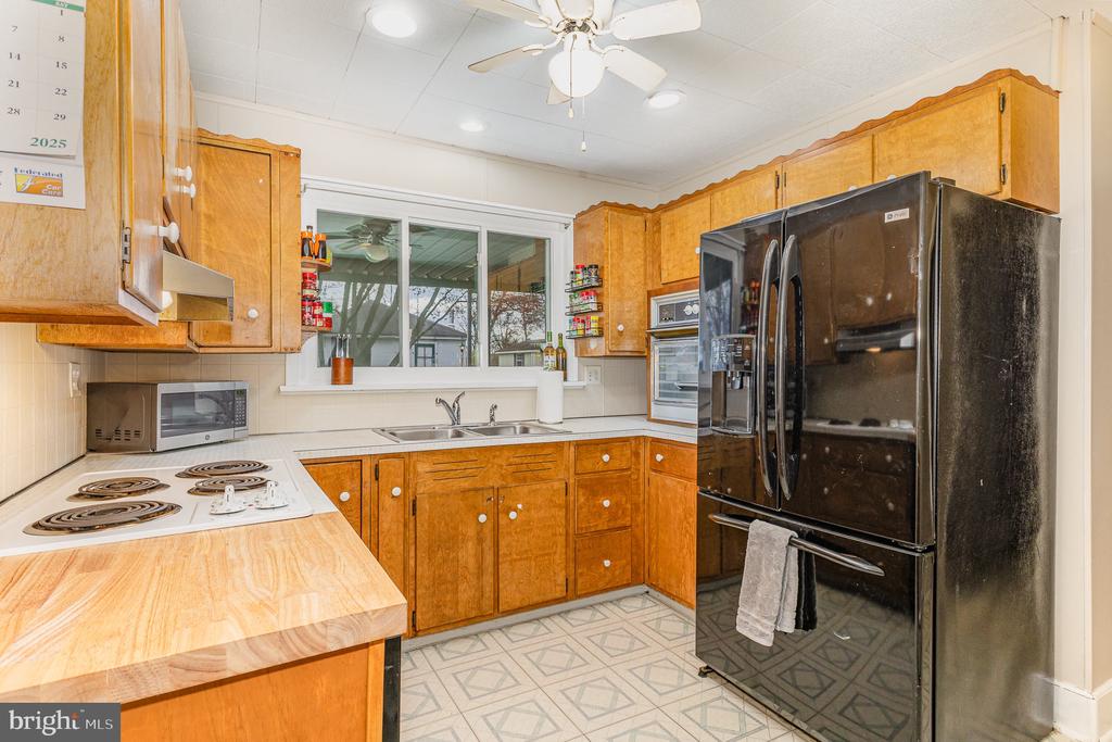 Kitchen with honey-colored wood cabinets, a black refrigerator, and a double sink beneath a wide window.