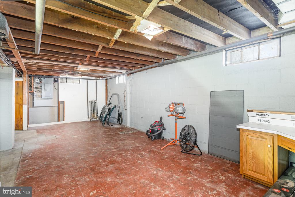Unfinished basement with exposed ceiling joists, utility equipment, and a small wooden cabinet.