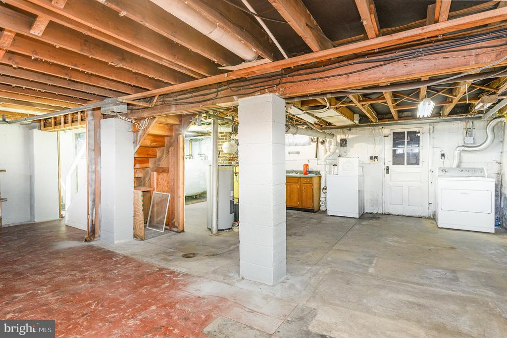 Unfinished basement with exposed joists, a central support column, and laundry appliances.
