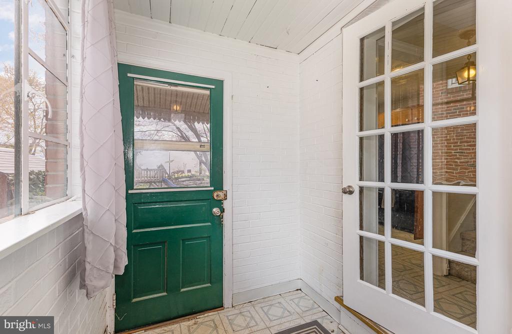 Entryway with a dark green front door, white brick walls, and patterned tile floor.