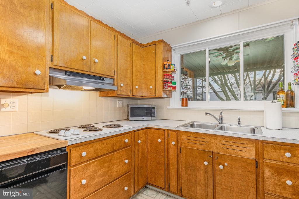 Kitchen with honey-colored wood cabinets, white counters, electric cooktop, and sink beneath a wide window.