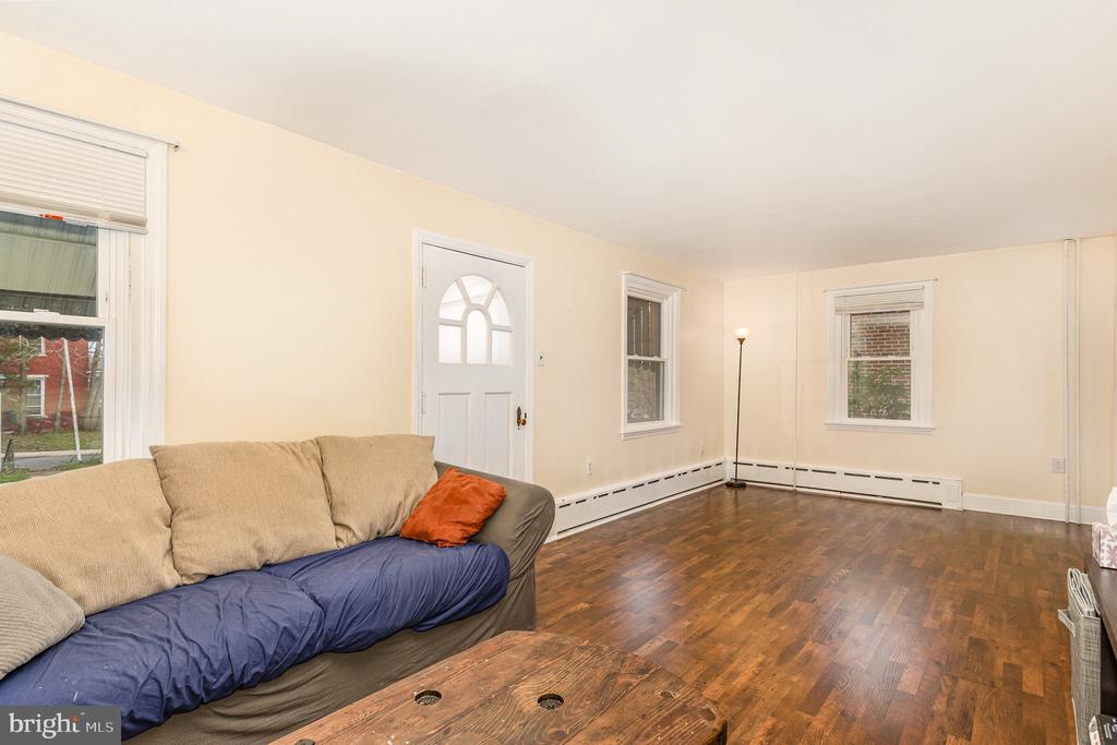Living room with hardwood floors, arched-window front door, and a beige sofa with colorful cushions.
