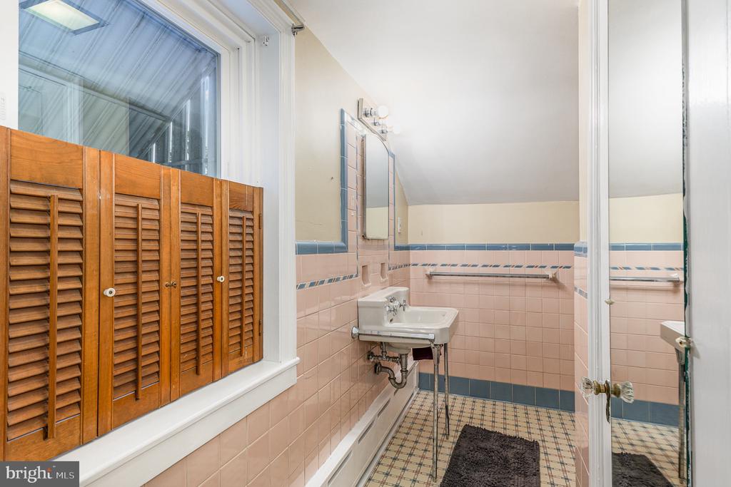 Bathroom with pink tile, patterned floor, pedestal sink, and wooden louvered window shutters.