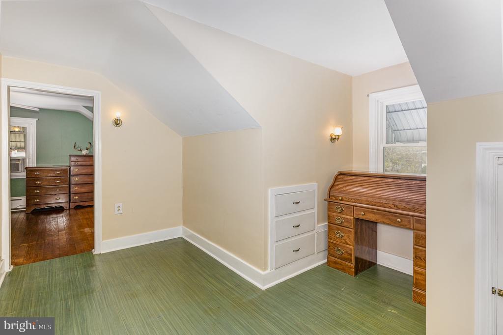 Bedroom with sloped ceilings, green flooring, white built-in drawers, and a wooden roll-top desk.