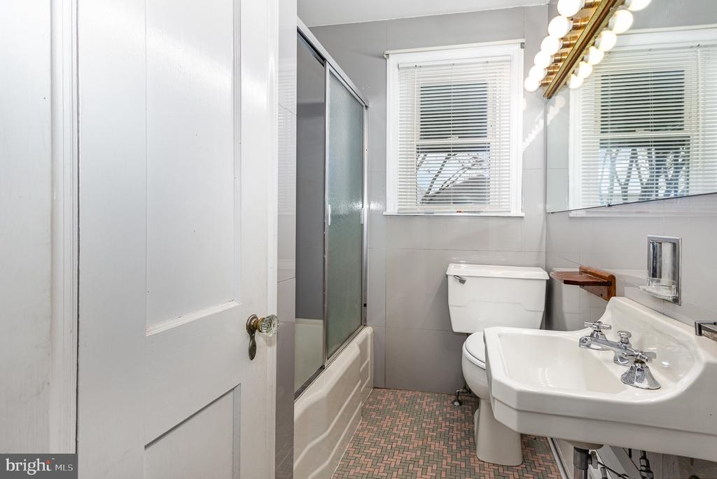 Bathroom with pedestal sink, tub-shower, toilet, and patterned tile floor.