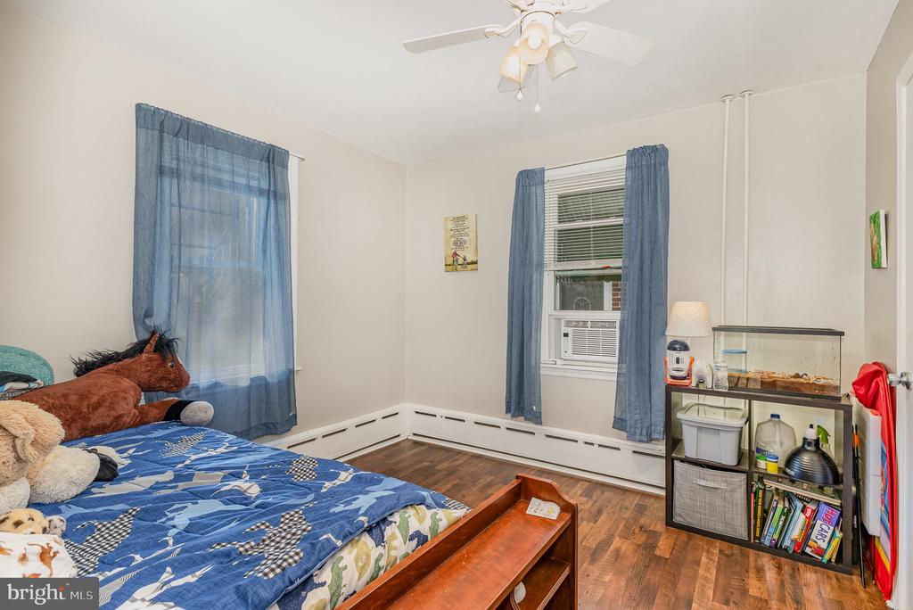 Bedroom with blue patterned bedding, blue curtains, window air conditioner, and hardwood floors.