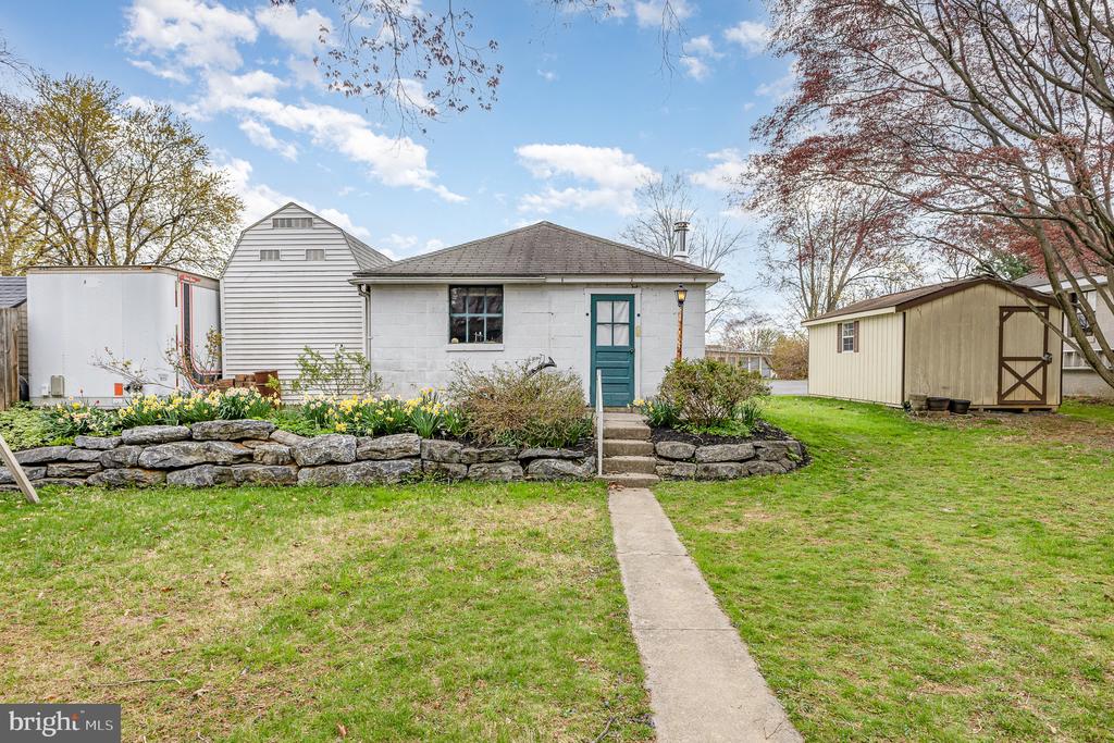 White house with a teal front door, stone retaining wall, and detached shed.