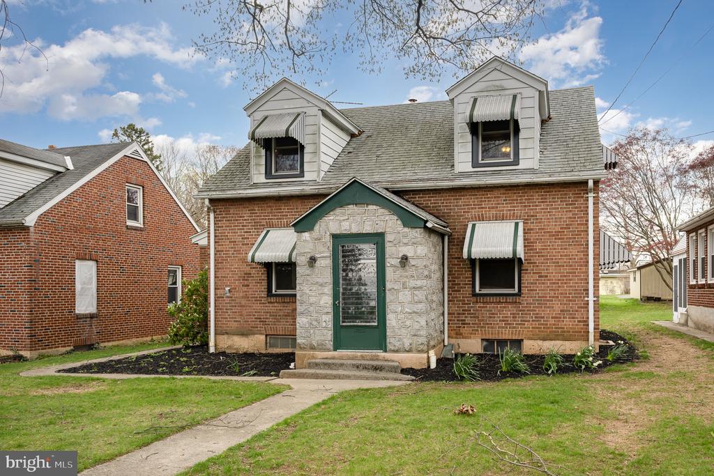 Red-brick house with a stone entry, green door, and two dormers with striped awnings.