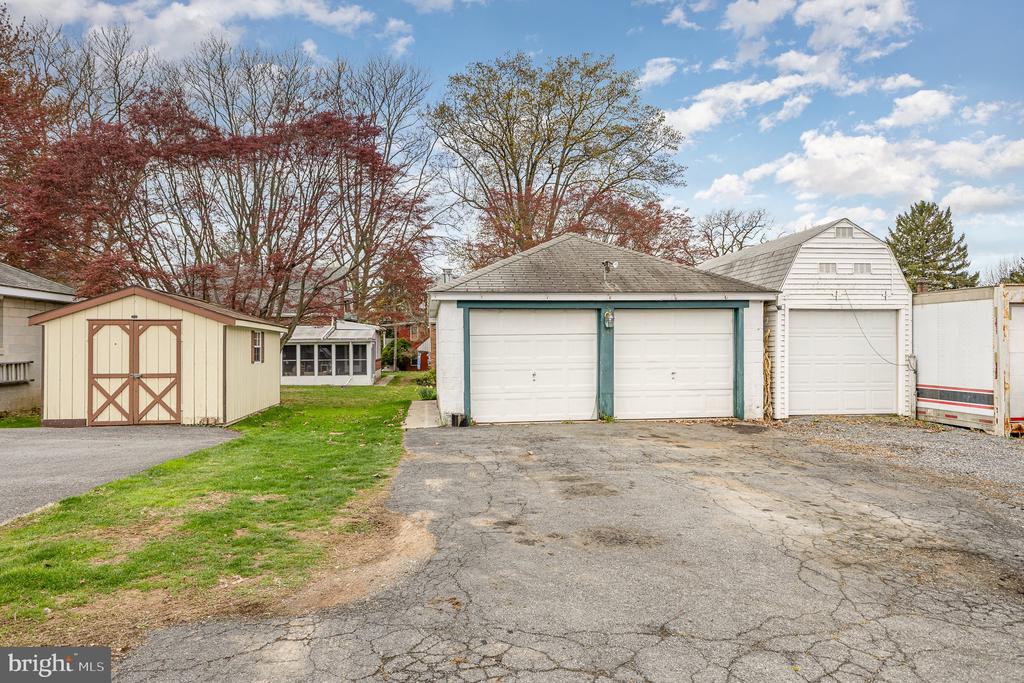 Detached garages and storage sheds line a cracked paved driveway.