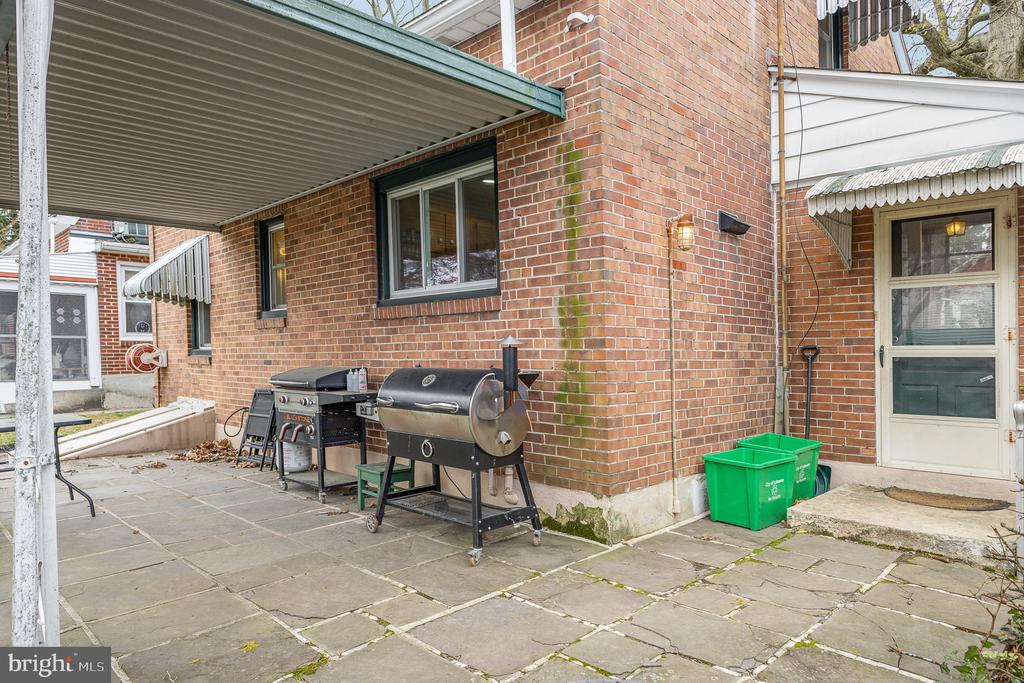Brick home patio with two grills beneath a covered canopy beside the side entrance.