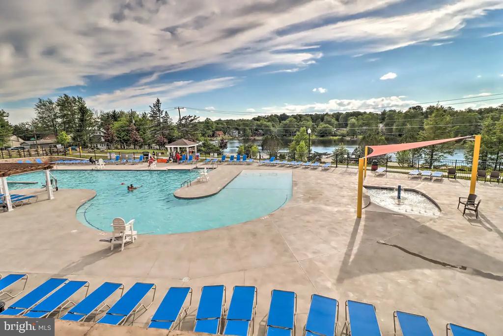 Community pool with blue lounge chairs and a lake beyond the fence.