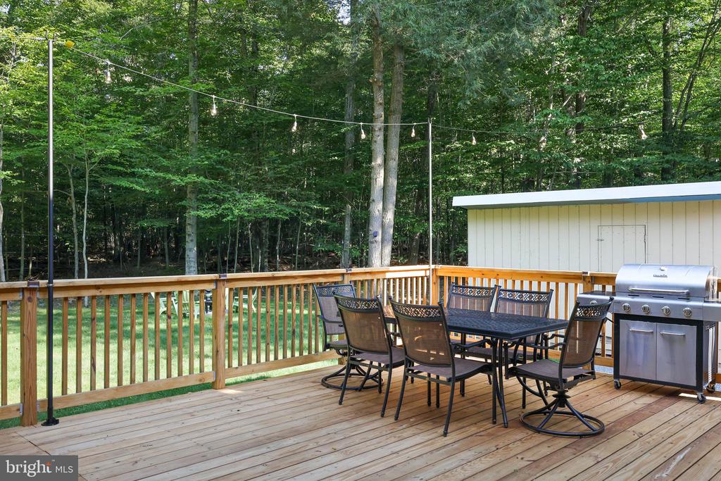 Wooden deck with outdoor dining set and grill overlooking a wooded yard.