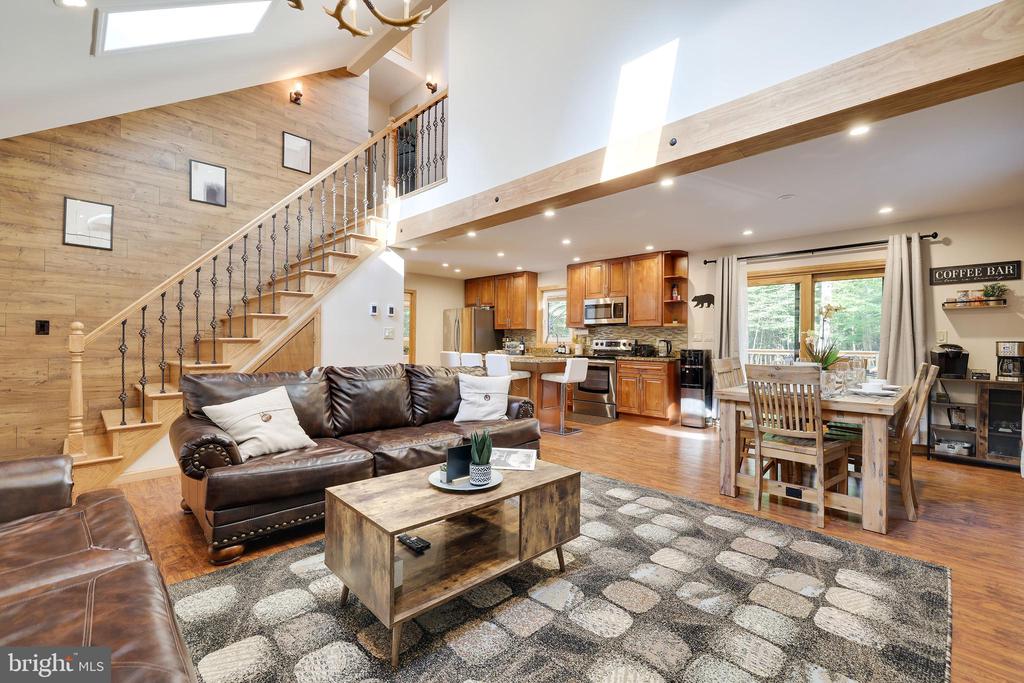 Open-plan living room with a leather sectional, vaulted ceiling, and wood-paneled staircase wall.