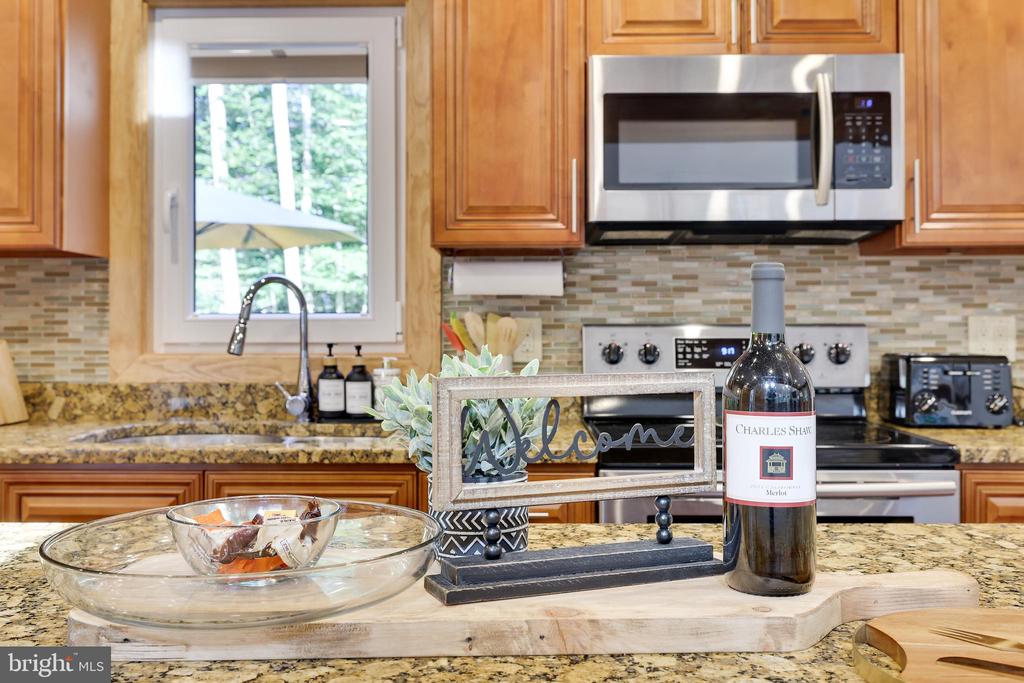 Kitchen with granite counters, warm wood cabinetry, stainless appliances, and a decorative welcome sign.