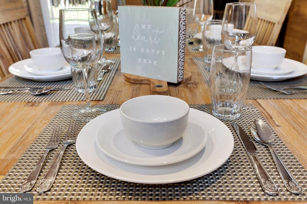 Dining table set with white dishes, woven placemats, glassware, and a “MY heart IS HAPPY HERE” sign.
