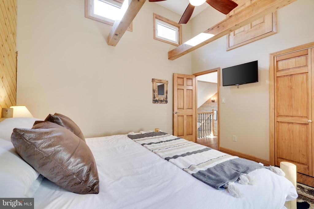 Bedroom with exposed wood ceiling beams, skylights, and a wall-mounted television.