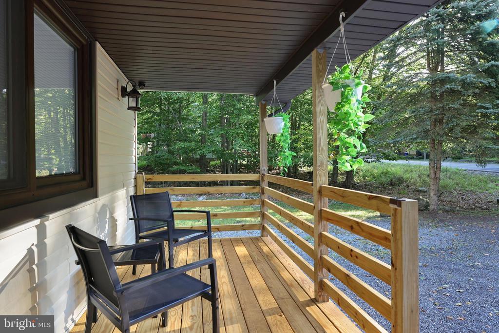 Covered wooden porch with two chairs and hanging plants overlooking a leafy yard.