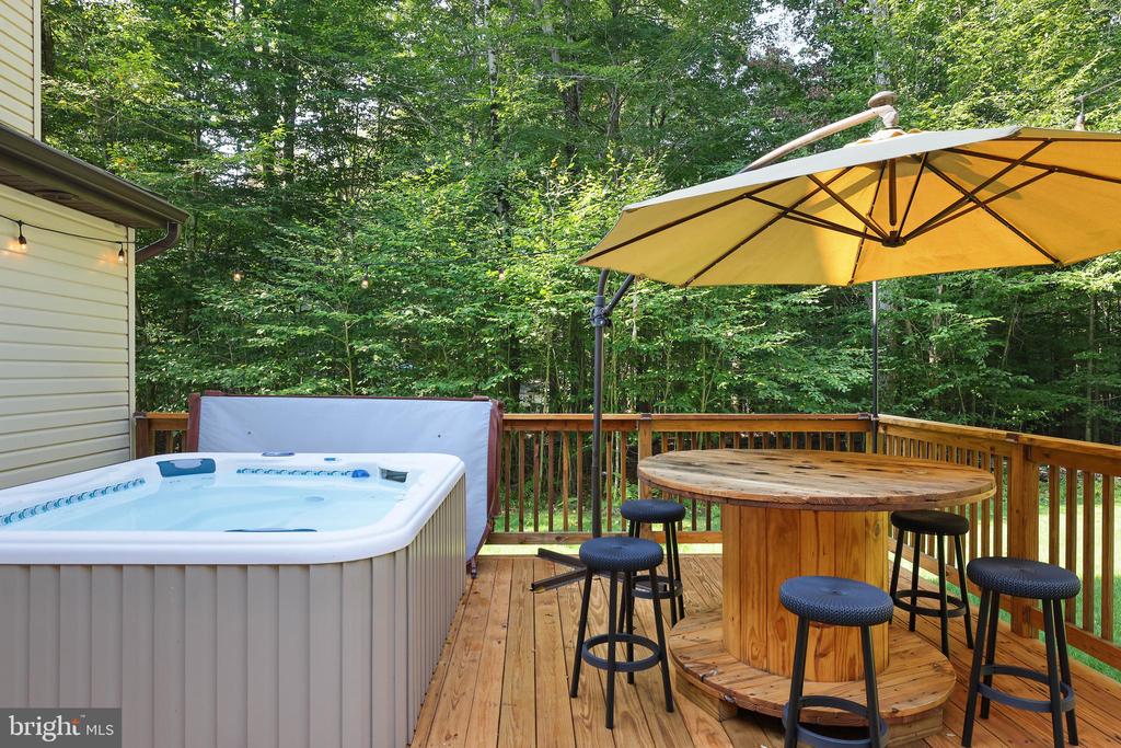 Wooden deck with a hot tub and umbrella-shaded table overlooking dense trees.