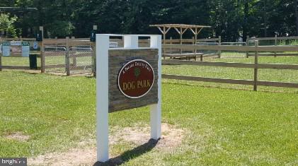 Dog park sign beside a fenced grassy area and wooden shelter.