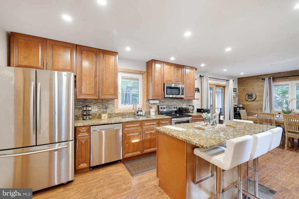 Kitchen with warm wood cabinets, stainless steel appliances, and a granite island with white barstools.