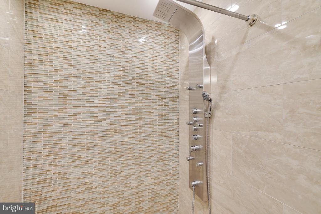 Bathroom shower with a rainfall showerhead, handheld wand, body sprays, and mosaic tile accent wall.