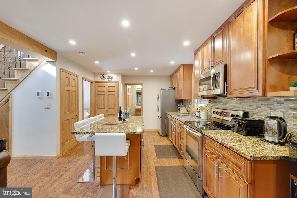 Kitchen with warm wood cabinets, granite counters, stainless appliances, and a breakfast bar with white stools.