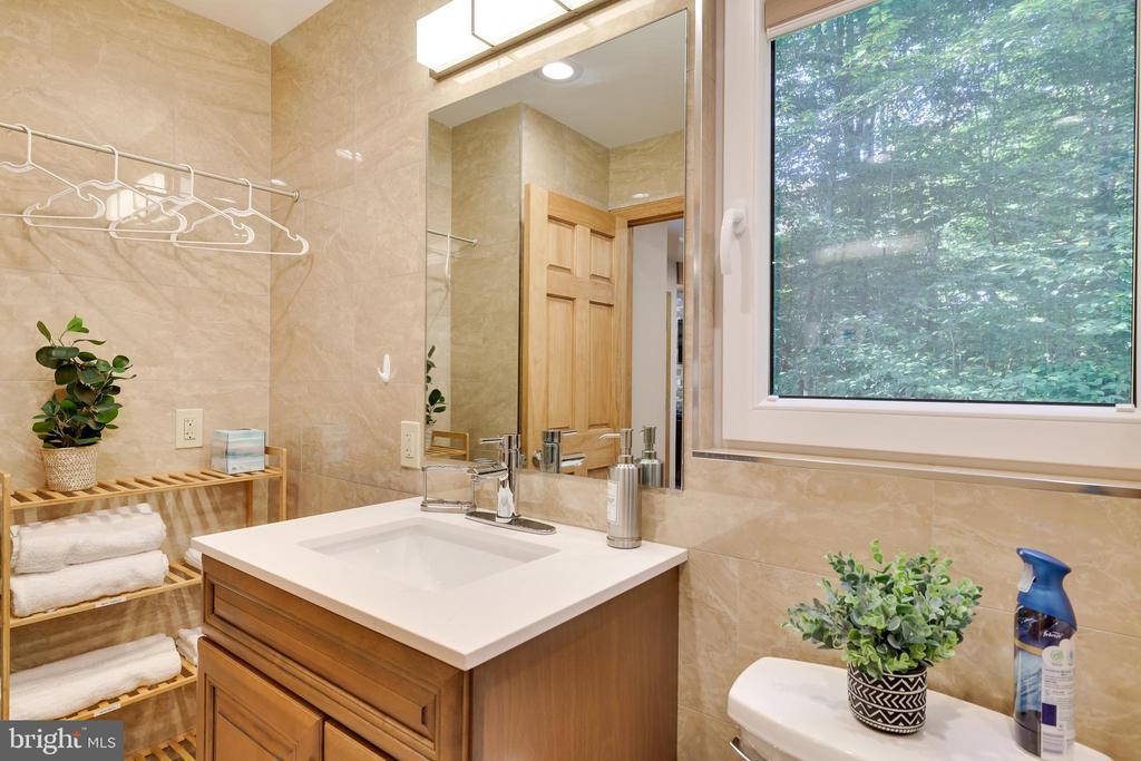 Bathroom with a wood vanity, beige tile, large mirror, and window overlooking trees.