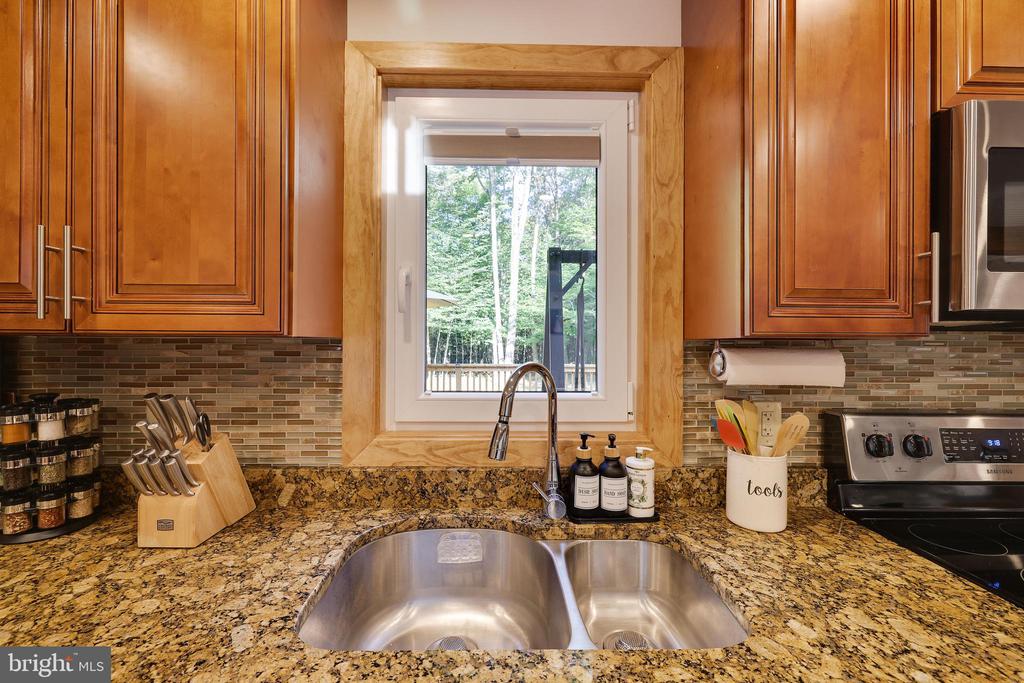Kitchen with granite counters, warm wood cabinets, and a double-basin sink beneath a window overlooking trees.