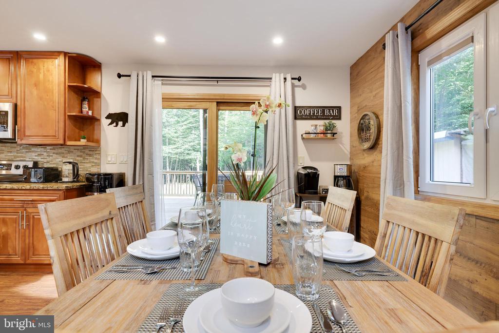Dining area with a set wooden table, honey-toned kitchen cabinets, and glass doors opening to a deck.
